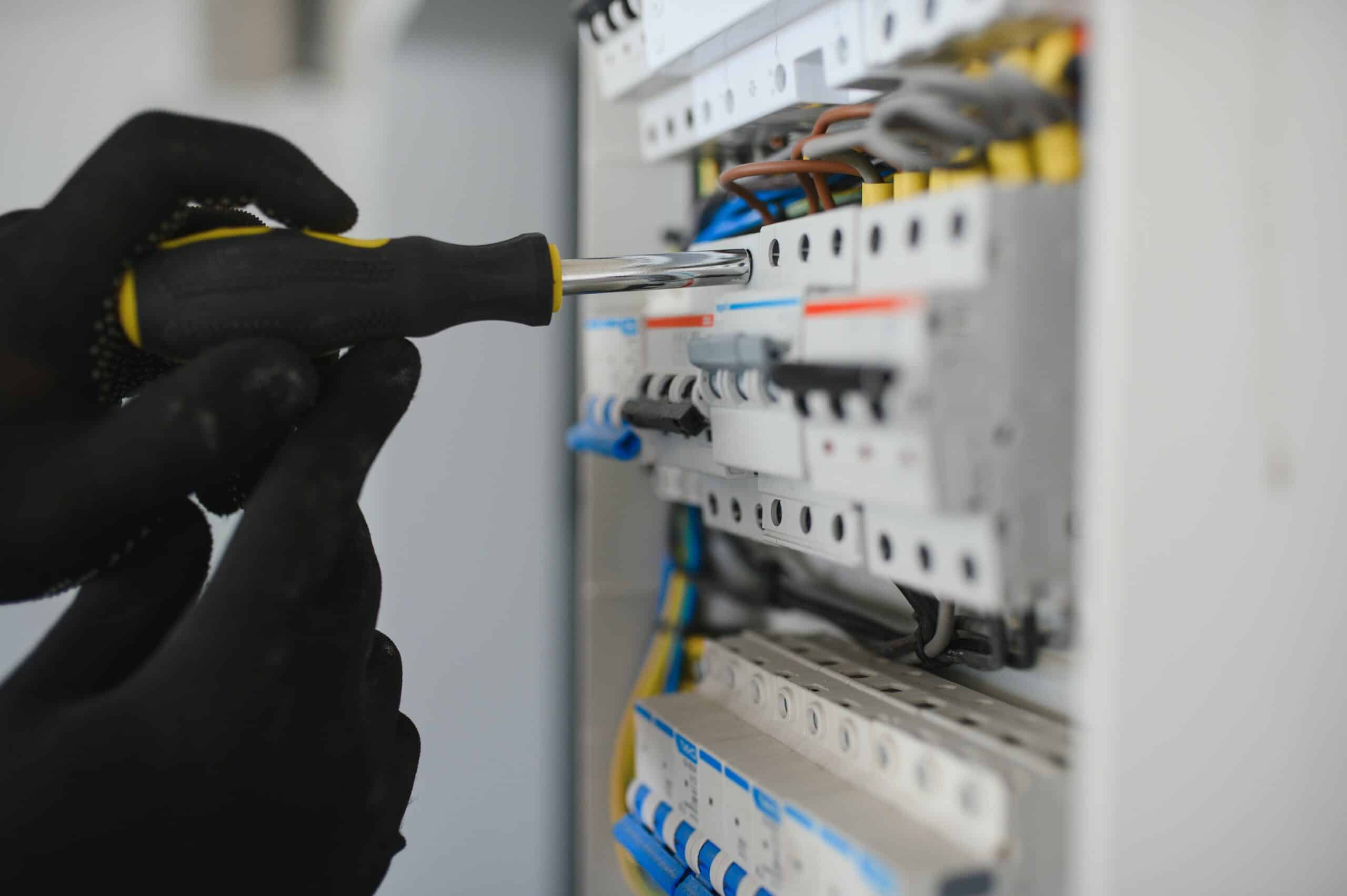 Main gantée avec tournevis travaillant sur un tableau électrique, installant ou réparant des disjoncteurs et fils.