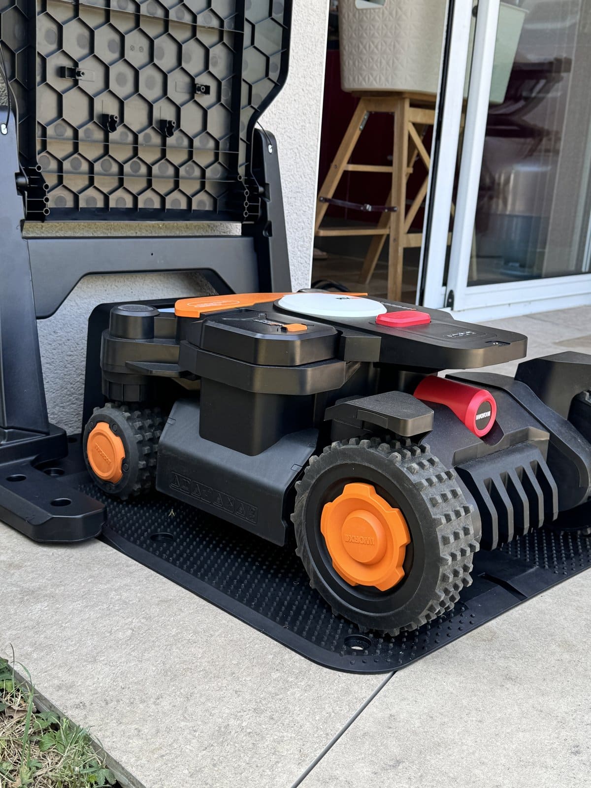 Robot tondeuse Worx Landroid noir et orange dans sa station de charge sur une terrasse extérieure.